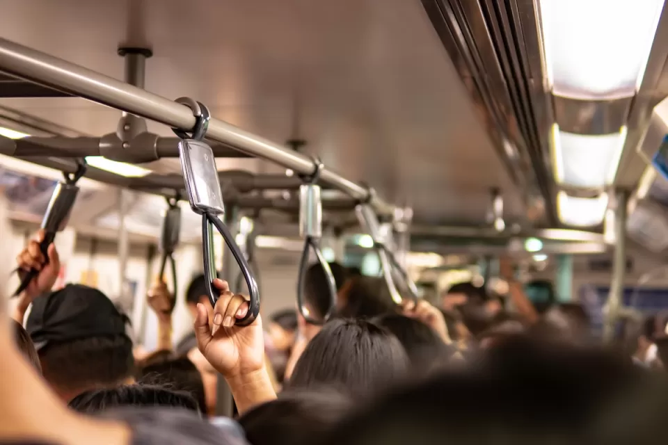 Close-up on passengers holding overhead straps on busy public transit bus.